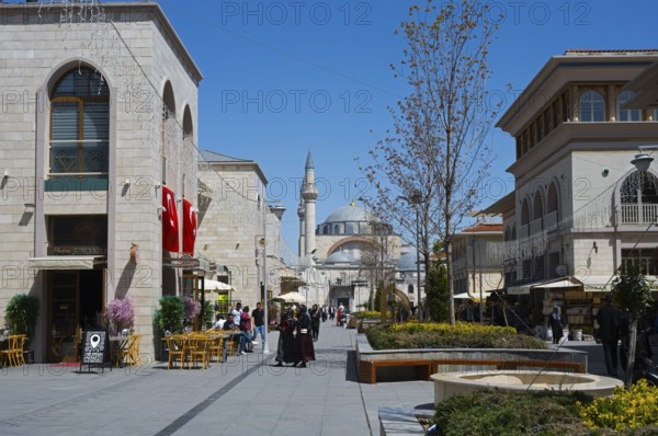 Lively shopping street with stylish buildings, mosque in the background and decorative lighting,