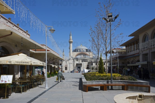 Wide pedestrian zone with shops and street cafés, a mosque in the background under a blue sky,