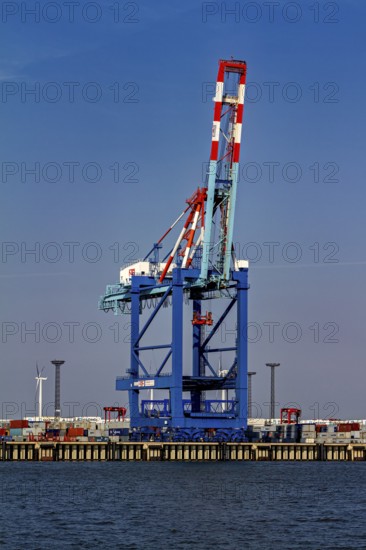A single blue port crane, stacks of containers and a wind turbine in the background, The cranes of