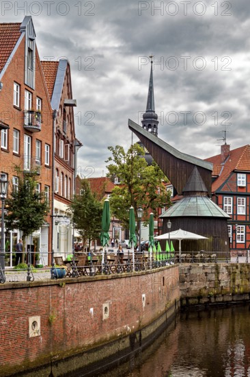 Timber crane and half-timbered houses with a tower on the riverbank under a dramatic sky, The old