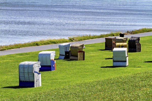 Beach chairs in different colors in a meadow next to a waterside road, beach chairs on the beach in