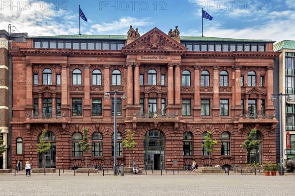 Historic bank building with red façade and two flags on the roof under a blue sky, The center of