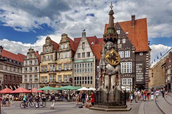 Lively city center with an impressive statue in front of historic buildings under a partly cloudy