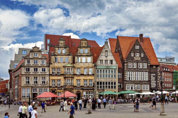 Historic old town with half-timbered houses and people on a busy market square under a blue sky,