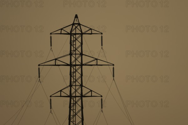 Electricity pylon and power lines silhouette at sunset, England, United Kingdom