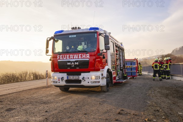 Firefighters stand by a fire truck on the side of the road at sunrise, ready for action, fire