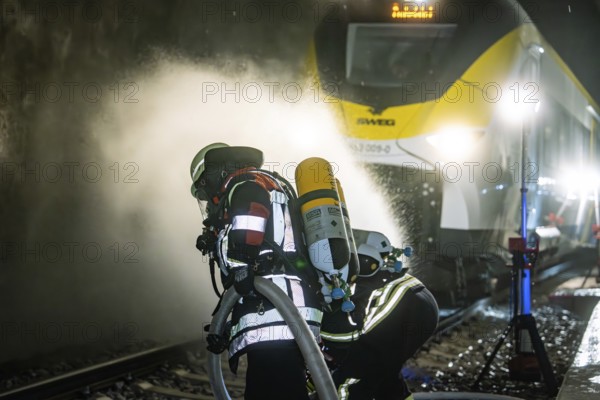 Firefighters wearing respiratory protection spray water on a train in a tunnel, fire brigade