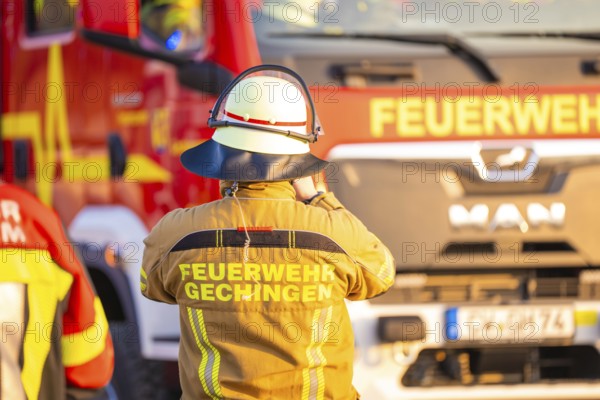 A firefighter stands in front of a fire truck wearing protective clothing, fire department exercise