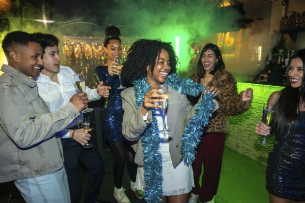 Group of diverse young adults having fun, dancing, and laughing while holding champagne flutes at a