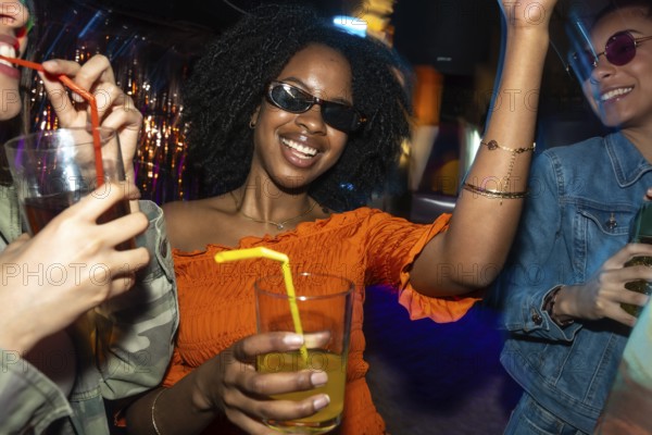 Young happy diverse women enjoying a night out, smiling and dancing together with drinks in a