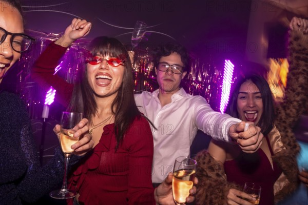 Young diverse friends dancing and cheering while holding glasses of alcoholic drinks, enjoying a