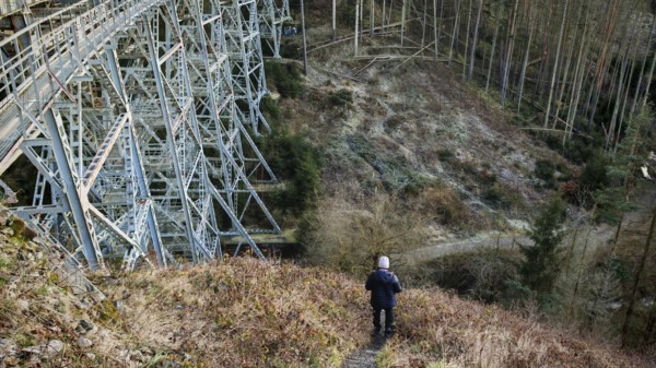 Hikers on a path next to a large metal-textured bridge, old railroad bridge in the forest,