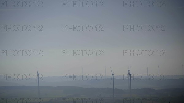 Blurred range of hills with isolated wind turbines in morning fog under blue sky, Franconian Forest