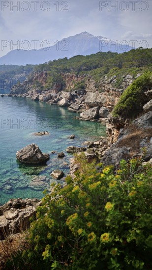 Rocky coast with turquoise water and a snow-capped mountain Tahtali Dagi in the background,