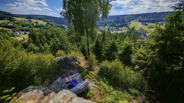 A panorama from a viewpoint with a person on a bench with a view of a picturesque valley,