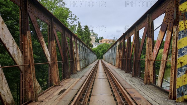 Old, rusty metal railroad bridge leads through green forests to a remote small town, Loket, Czech