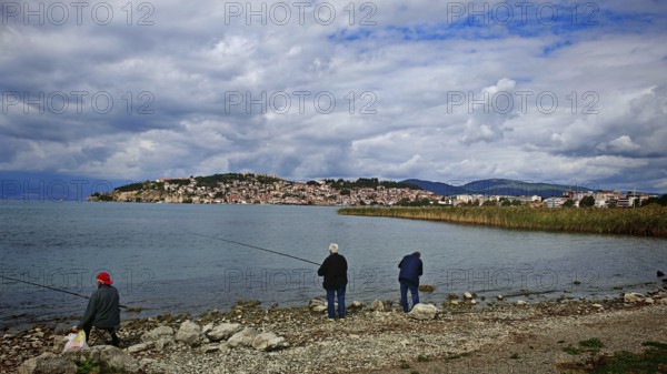 Fishermen on the shore of a lake with a view of a city in the background under cloudy sky, Ohrid,