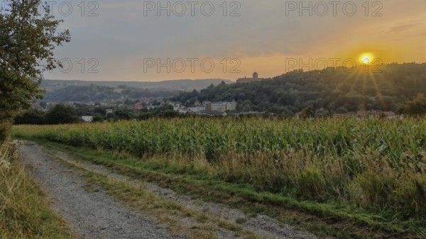 A trail leads along fields with a village in the background at sunset, Kronach with a view of