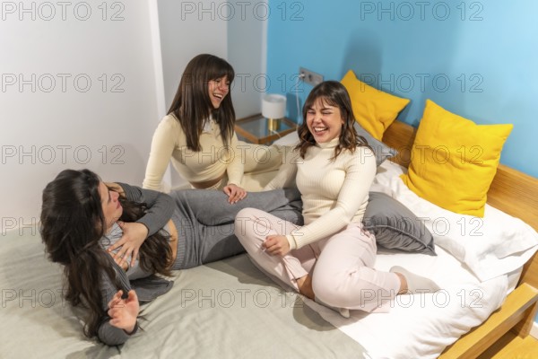Three cheerful young women friends are enjoying a slumber party, laughing heartily while relaxing