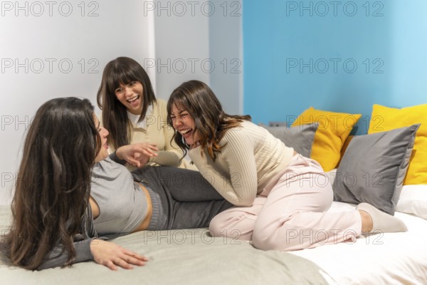 Three young women friends spending time together laughing and enjoying a slumber party on a bed