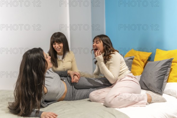 Three young women relaxing and enjoying a cheerful sleepover on a comfortable bed in a brightly