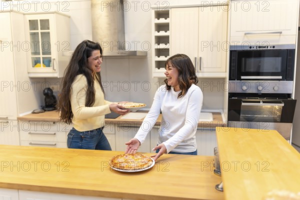 Two cheerful women are happily sharing a delicious homemade pizza in a modern kitchen, enjoying a