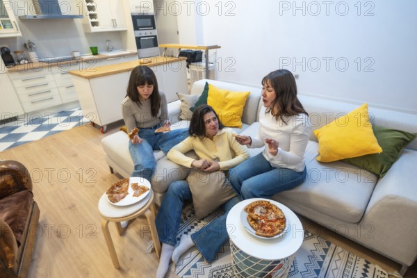 Three young women gather on a comfortable sofa in a modern living room, sharing pizza slices and