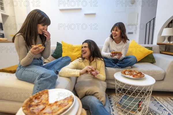 Three young women relaxing on a couch and floor, sharing pizza slices during a casual gathering,