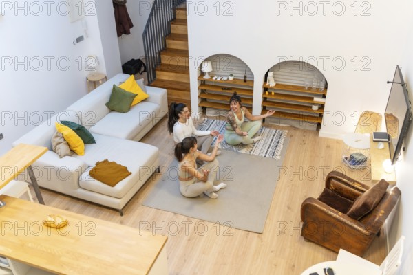 Three young women sitting in a living room, smiling and relaxing on yoga mats, enjoying a peaceful