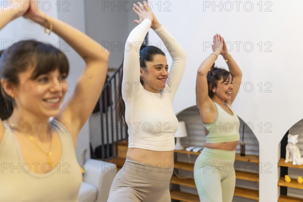 Three diverse women practicing yoga together at home, smiling and balancing in a sunlit modern
