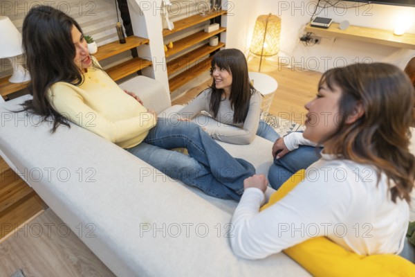 Pregnant woman relaxing on a sofa with two close friends in a cozy living room, sharing laughter,