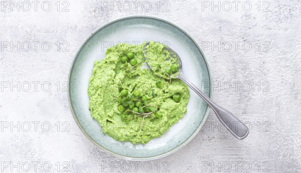 A vibrant green pea puree fills a shallow bowl, topped with fresh peas and microgreens. The dish