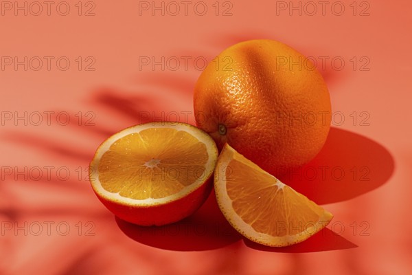 On the coral surface, next to two neatly sliced slices, there is a whole orange. Sunlight casts