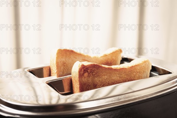 Two slices of bread are toasting in a shiny metal toaster, set on a countertop in a warm kitchen.