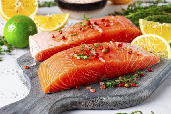 Two pieces of salmon fillet sit on a wooden cutting board. They are topped with herbs and pink