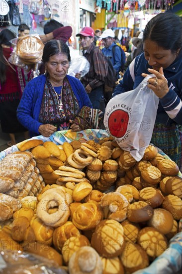 Mayan woman in traditional clothing buys bread at the market in Sololá, Highlands, Sololá