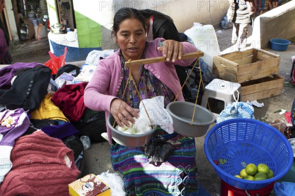 Mayan woman in traditional clothing weighs with a hand scale at the market in Sololá, Highlands,