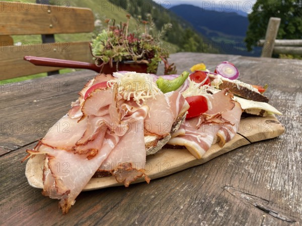 Typical snack on the alpine pasture, bacon bread and cheese bread on wooden plate on wooden table,