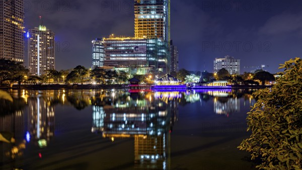 At night, illuminated modern buildings and a temple are reflected in the tranquil lake, The Seema
