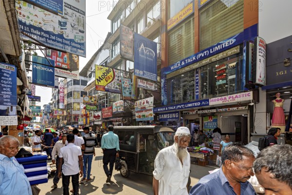 Populated street with shops and eye-catching advertising posters under clear skies, the hustle and