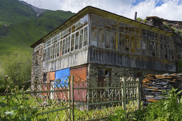 Old-fashioned house with a glass veranda against a mountain backdrop. Rustic atmosphere in green
