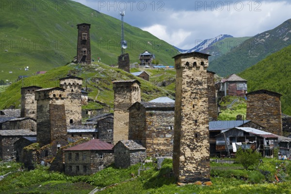 Historic mountain village with distinctive stone towers surrounded by green hills under a cloudy