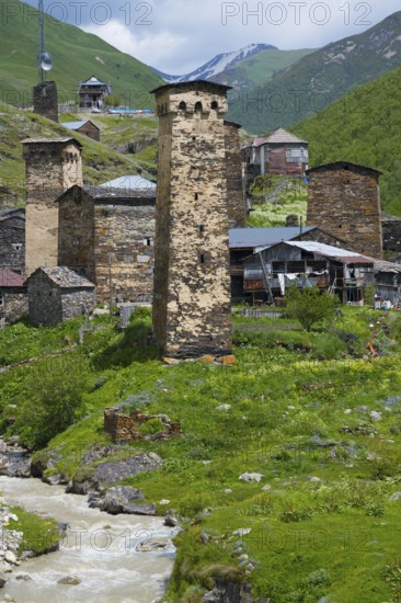 Mountain village with old stone towers on a river, nestled in a green alpine environment, defensive