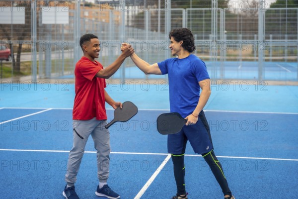 Two smiling male pickleball players of different ethnicities shaking hands on a vibrant blue court