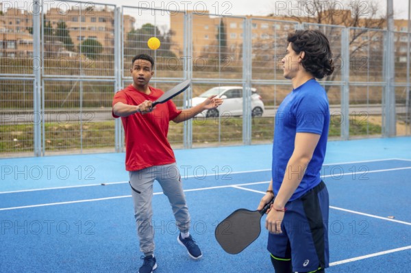 Young men enjoying a game of pickleball, one hitting the ball with a paddle on a vibrant blue