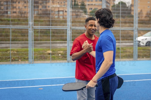 Two young multi ethnic men shaking hands and smiling on a blue pickleball court after a match,