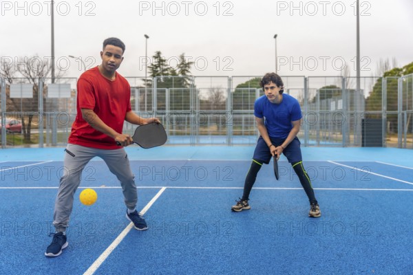 Two young men actively engaged in a pickleball game on an outdoor blue court, holding rackets and