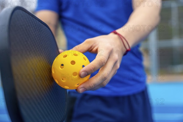 Hands holding a yellow pickleball and paddle on an outdoor court, poised to serve or dinkclose up