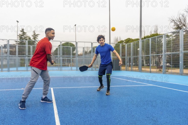 Two young menone african american, one caucasiancompete in an energetic outdoor pickleball rally,