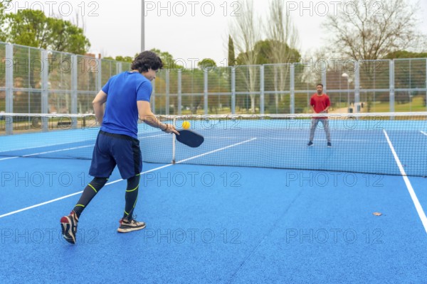 Two male athletes playing an intense pickleball game on a vibrant blue court, hitting the ball over
